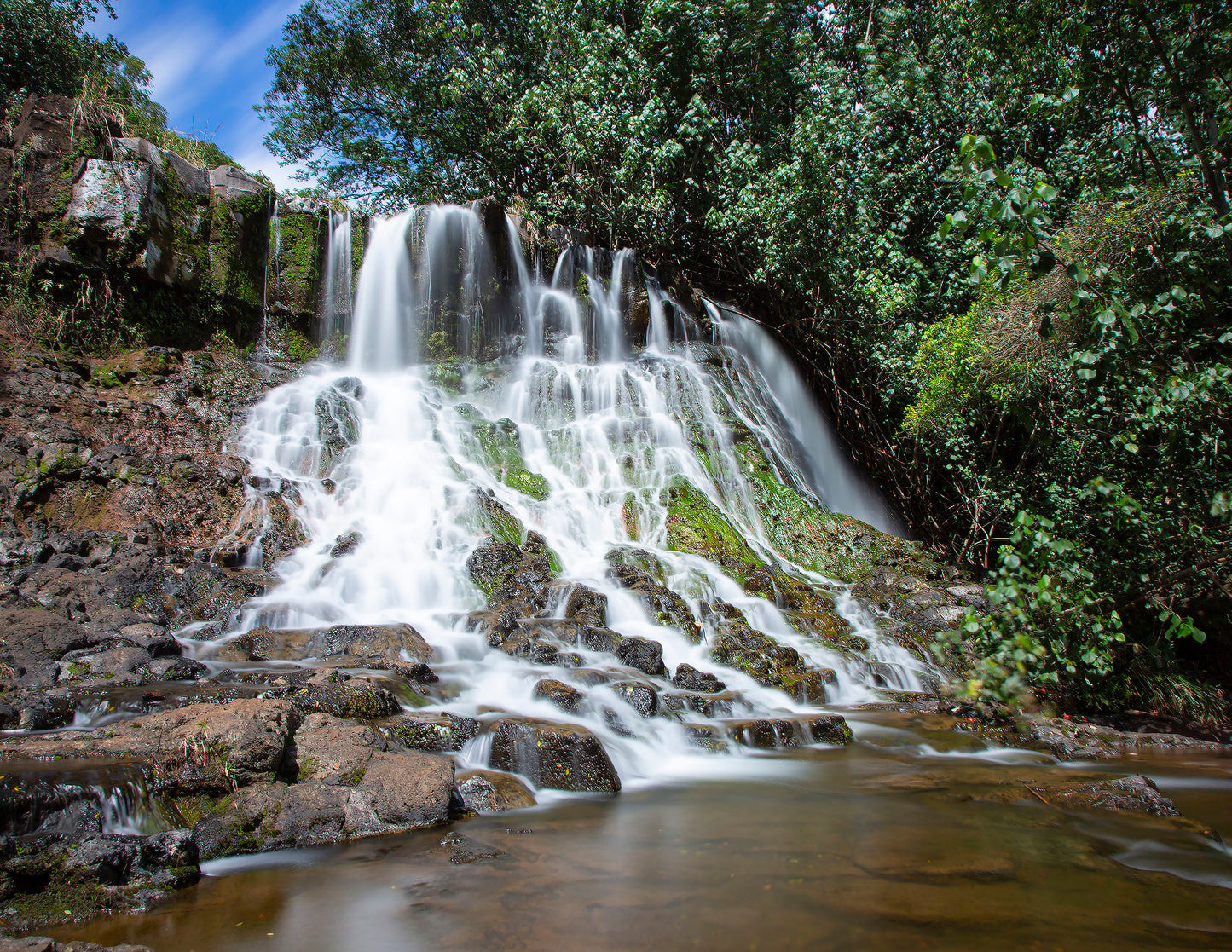 Fine art photograph of Hoopii Falls on Kauai. The water  rolls down a stepped cliff side to create an idyllic small waterfall and shallow pool. Landscape photography by Inspiring Images Hawaii.