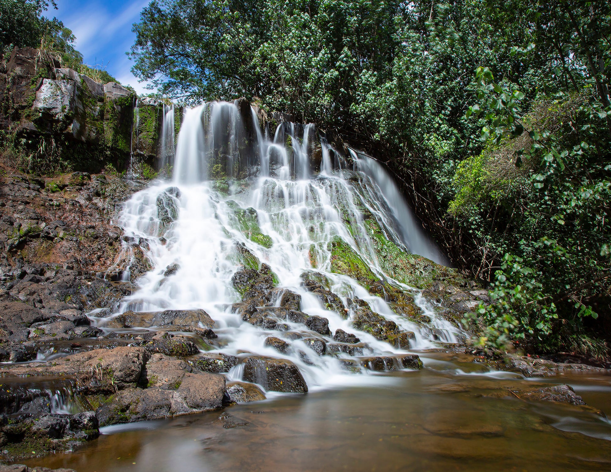 Fine art photograph of Hoopii Falls on Kauai. The water  rolls down a stepped cliff side to create an idyllic small waterfall and shallow pool. Landscape photography by Inspiring Images Hawaii.