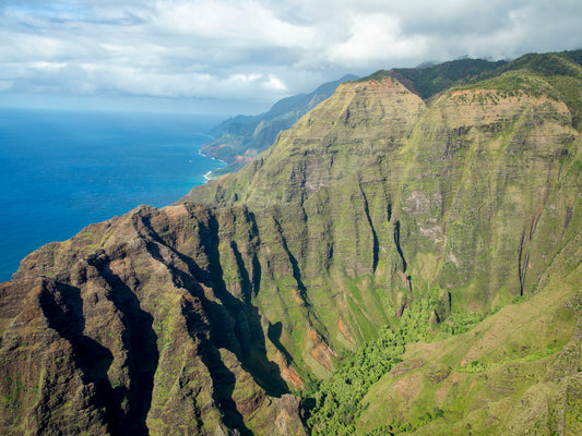Fine art photograph of Nualolo Valley, one of the valleys along Kauai’s Napali Coast. Steep, green cliffs drop down to the ocean with a waterfall  in the distance. Landscape photograph by Inspiring Images Hawaii.