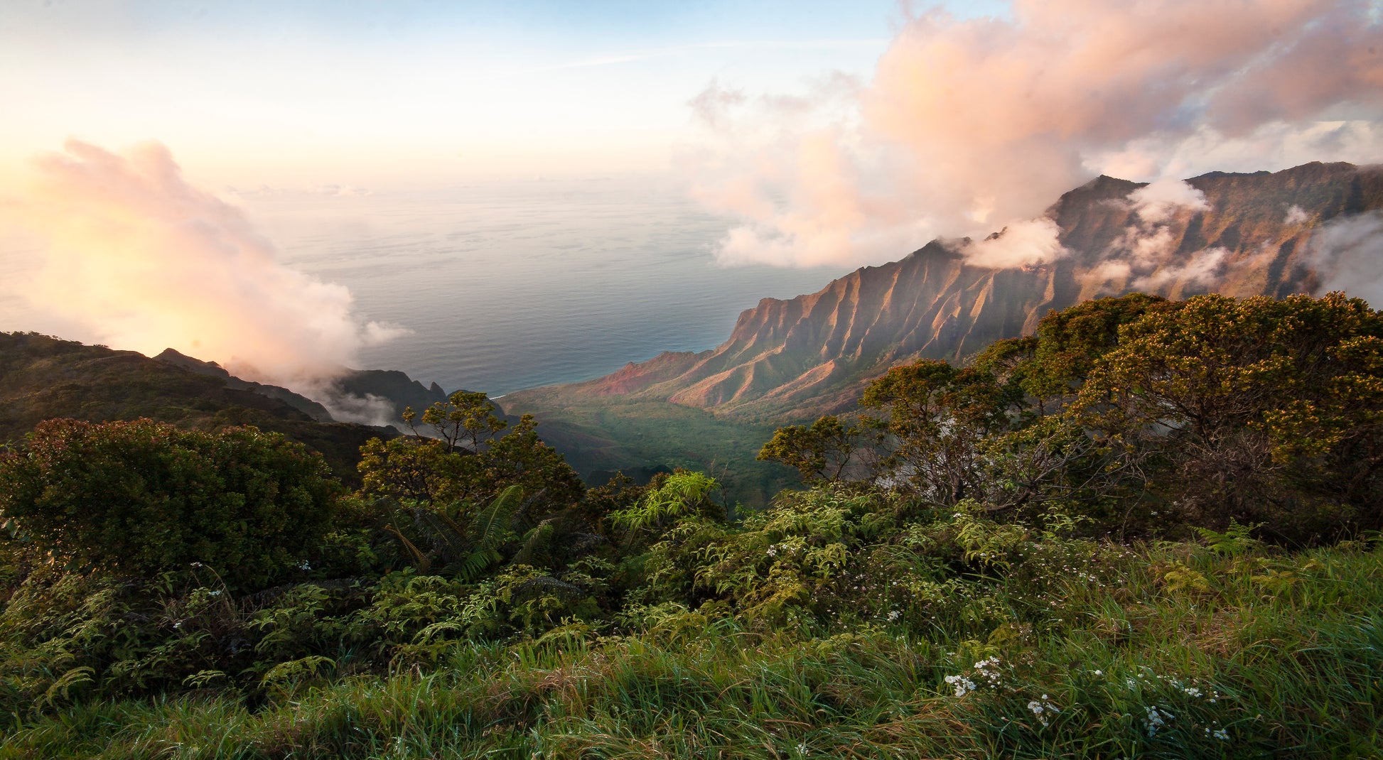 Fine art photograph of Kauai’s Kalalau Valley, taken at sunset. Pink hued clouds and rugged cliffs frame the valley with a calm ocean in the background. Landscape photography by Inspiring Images Hawaii.