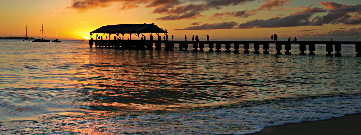 Fine art photograph of Kauai’s Hanalei Pier at sunset. An orange and pink sunset silhouettes the landmark pier in Hanalei Bay. Landscape photography by Inspiring Images Hawaii.
