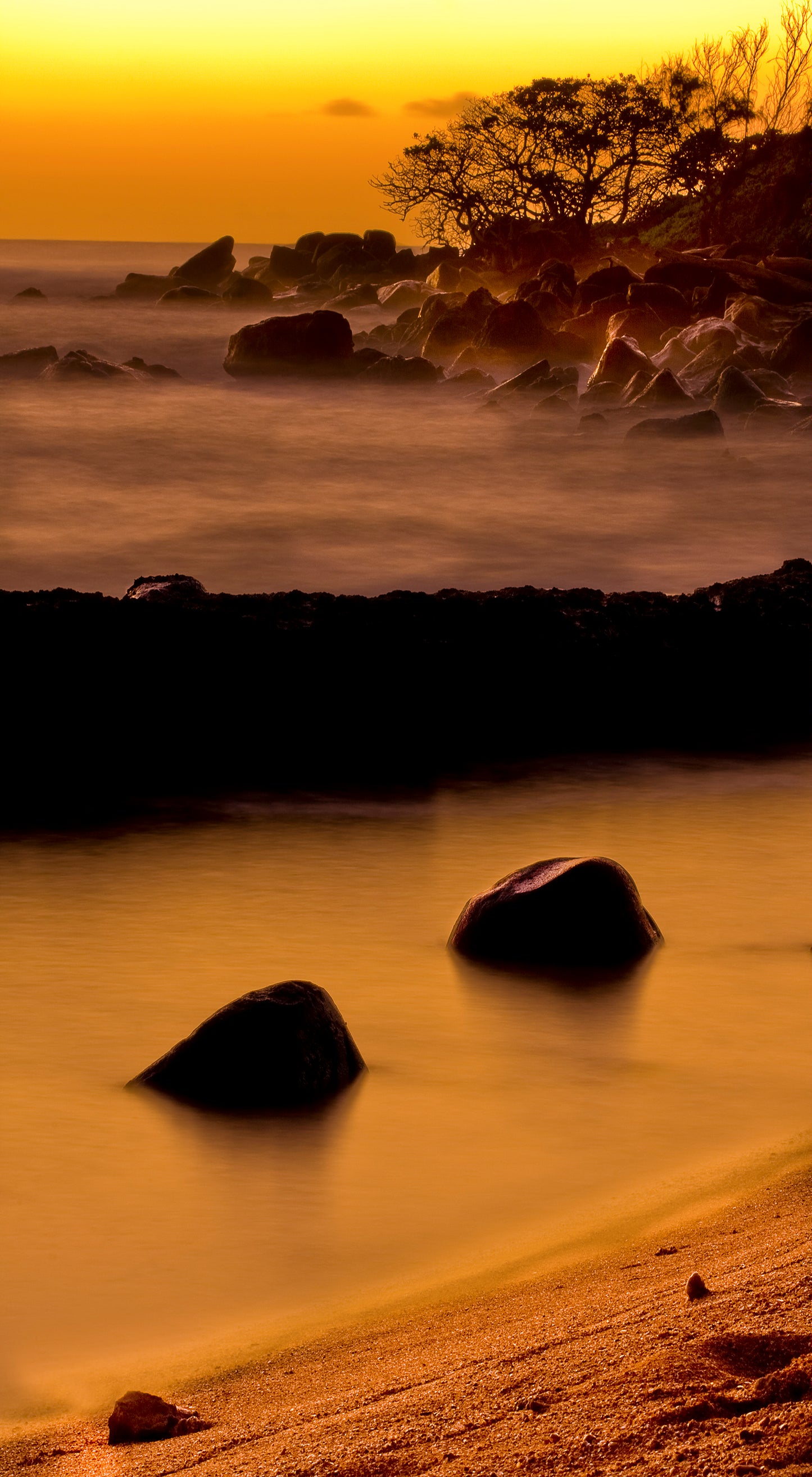 The sky and ocean glow orange at sunrise at a rocky beach on Kauai. Fine art landscape photograph by Inspiring Images Hawaii.