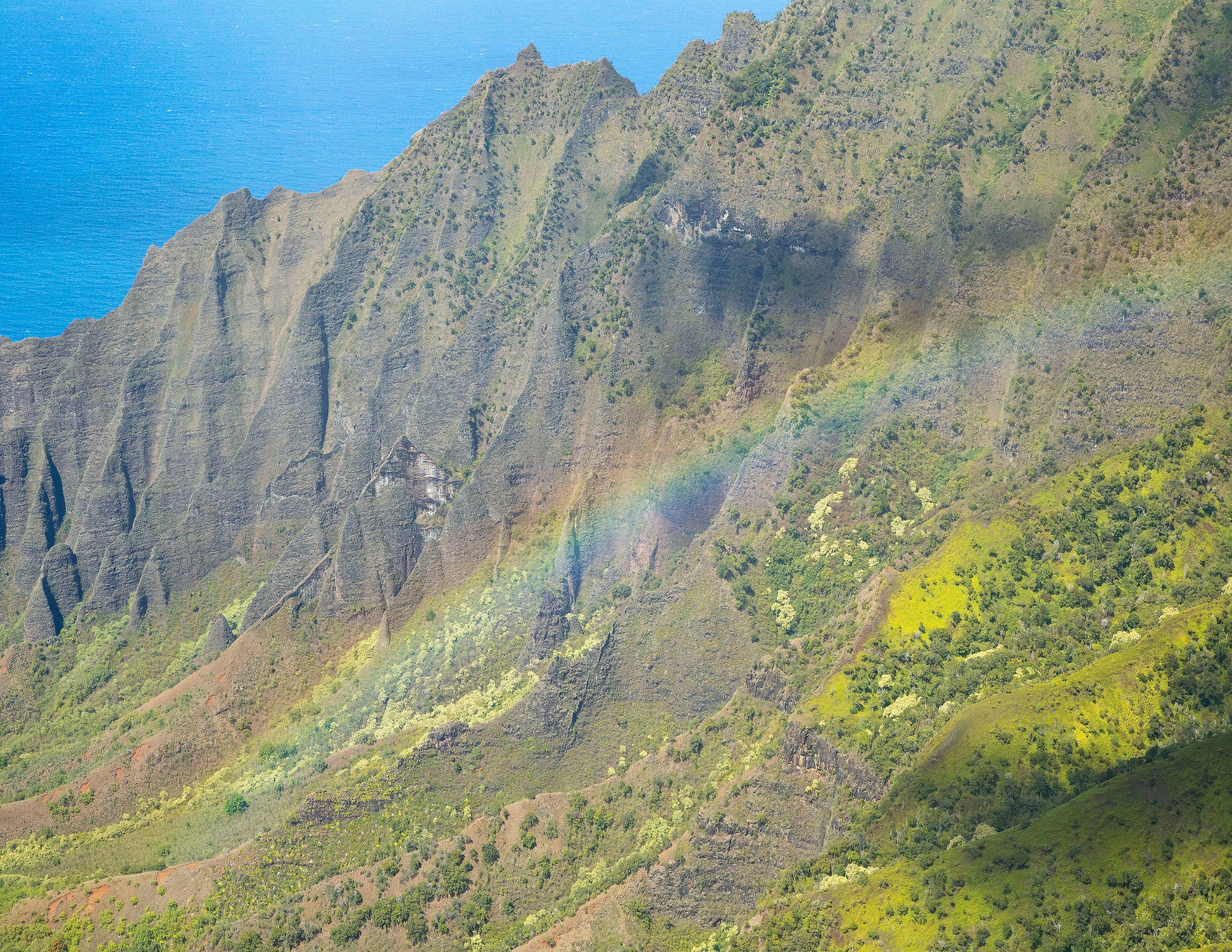 A rainbow stretches in front of a close up shot of Kalalau Valley’s cliffs. Fine art photograph by Kauai outdoor and landscape photographers Inspiring Images Hawaii.