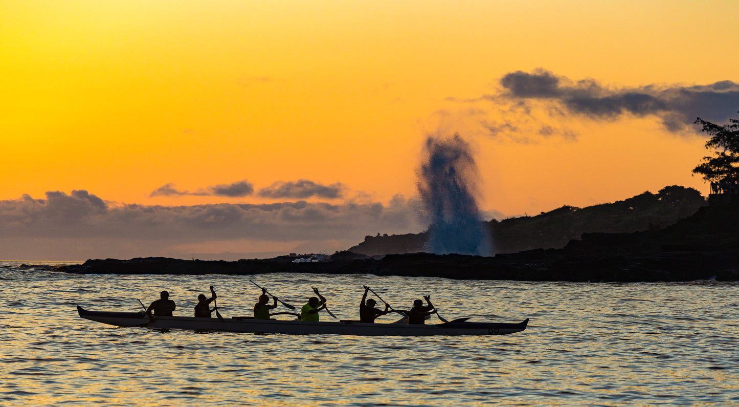Fine art photograph of Kauai’s Spouting Horn during a bright orange sunset with an outrigger canoe paddling in front of it. Taken by outdoor and landscape photographers Inspiring Images Hawaii.