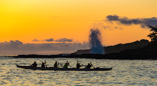Fine art photograph of Kauai’s Spouting Horn during a bright orange sunset with an outrigger canoe paddling in front of it. Taken by outdoor and landscape photographers Inspiring Images Hawaii.